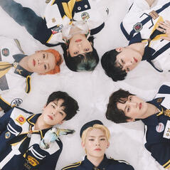 ONF members wearing scout uniforms lying in the snow with their heads together in a circle. From the popping album concept photos